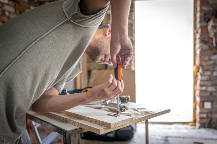 A man is screwing in a screw, a self-tapping screw for wood.