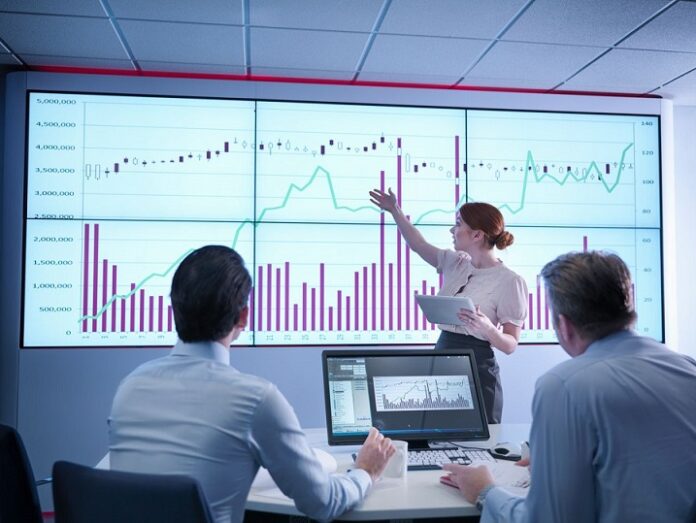 Businesswoman making presentation to colleagues in front of graphs on screen